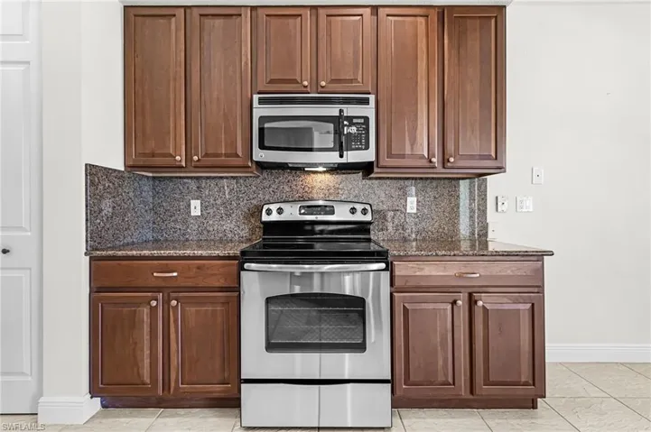 Kitchen featuring stainless steel appliances, backsplash, dark stone counters, and wood finish cabinets