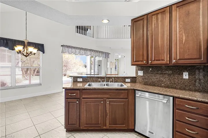 Kitchen with a peninsula, stainless steel dishwasher, hanging lights, light tile patterned floors, and decorative backsplash