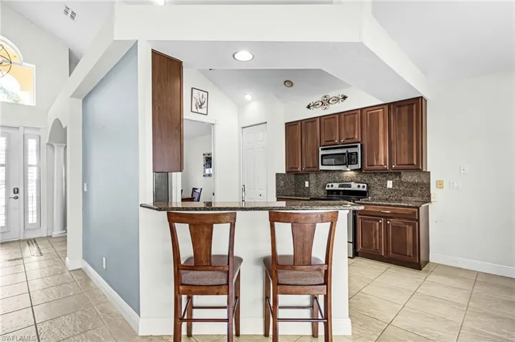 Kitchen with a breakfast bar, dark stone countertops, stainless steel appliances, a peninsula, and backsplash