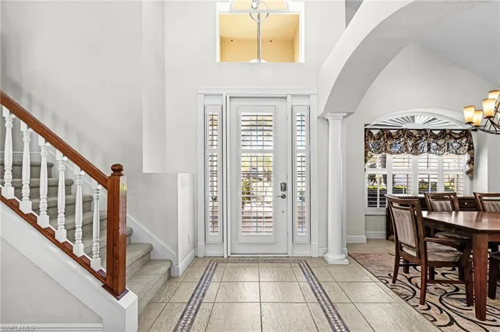 Entrance foyer with inlaid floor details, hanging lights, decorative columns, arched walkways, and a high ceiling