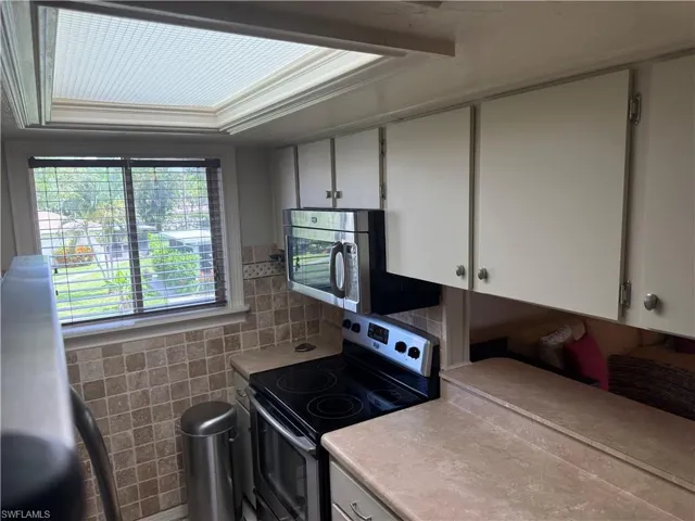 Kitchen area featuring a window with horizontal blinds, a tiled backsplash, overhead cabinetry, a built-in microwave, and an electric range
