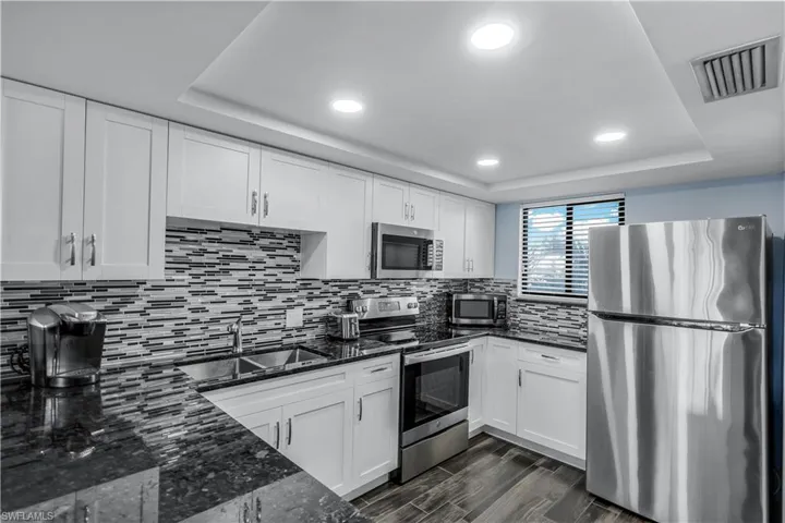 Kitchen featuring appliances with stainless steel finishes, a raised ceiling, dark stone counters, recessed lighting, and white cabinetry