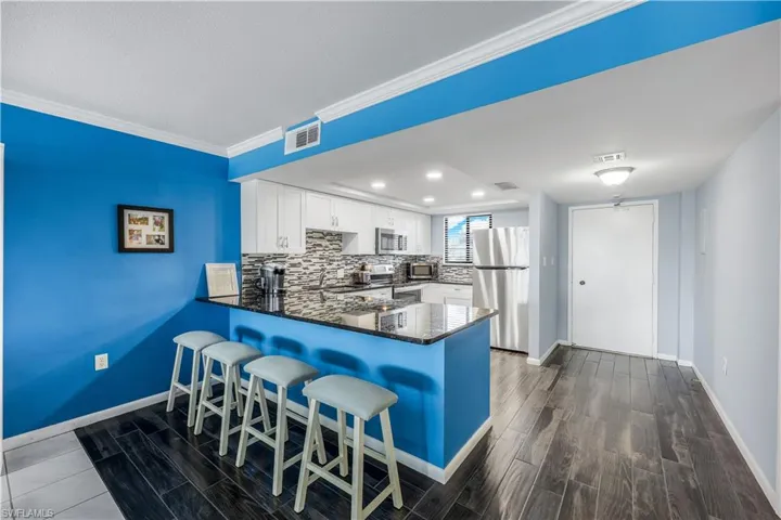 Kitchen featuring stainless steel appliances, a peninsula, white cabinets, dark wood finished floors, and a kitchen breakfast bar