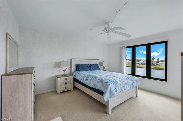 Bedroom featuring light colored carpet, a water view, a ceiling fan, and wallpapered walls