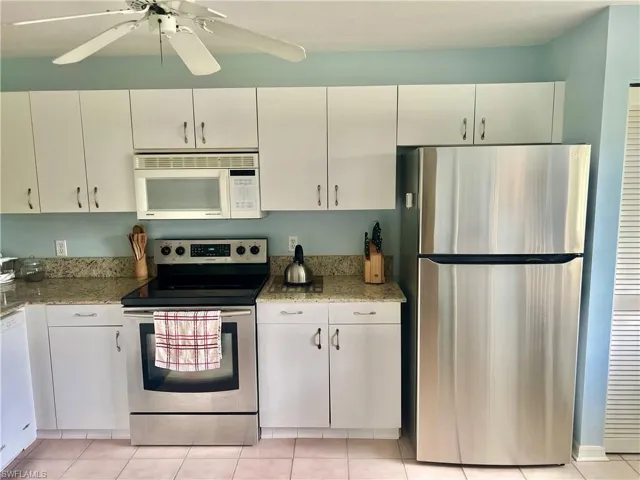 Kitchen with white cabinets, appliances with stainless steel finishes, light stone counters, and ceiling fan