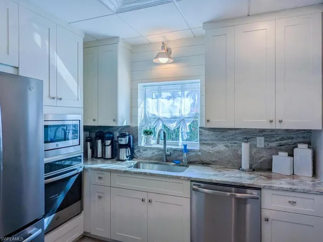 Kitchen with backsplash, sink, white cabinets, and stainless steel appliances
