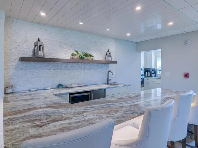 Bar with white cabinetry, stainless steel oven, sink, light stone counters, and decorative backsplash
