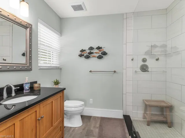 Bathroom with tiled shower, hardwood / wood-style floors, vanity, and toilet