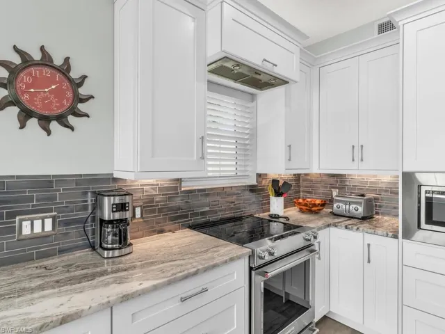 Kitchen featuring stainless steel appliances, white cabinetry, tasteful backsplash, and light stone counters