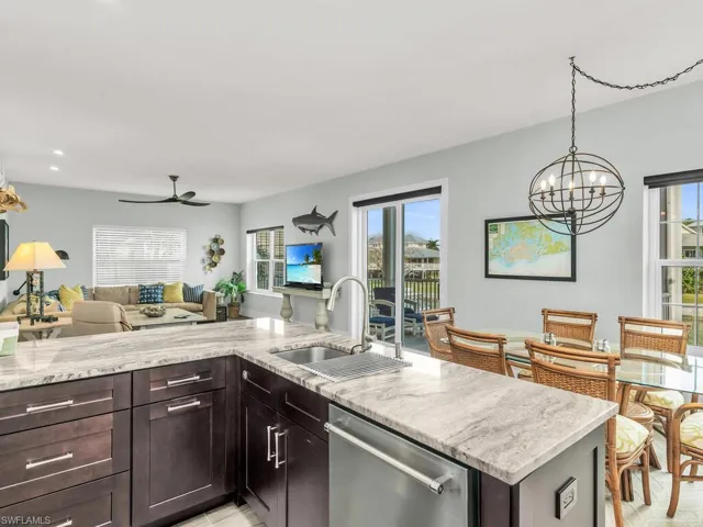 Kitchen featuring dishwasher, ceiling fan with notable chandelier, sink, light stone countertops, and dark brown cabinetry