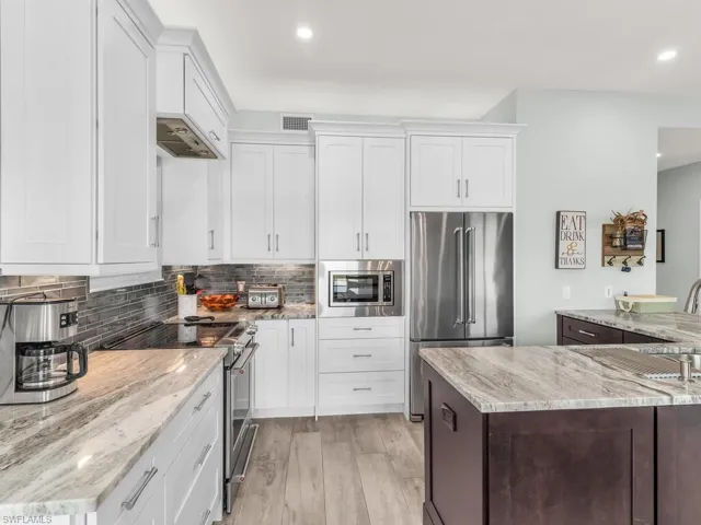 Kitchen featuring white cabinets, light hardwood / wood-style flooring, decorative backsplash, light stone countertops, and appliances with stainless steel finishes