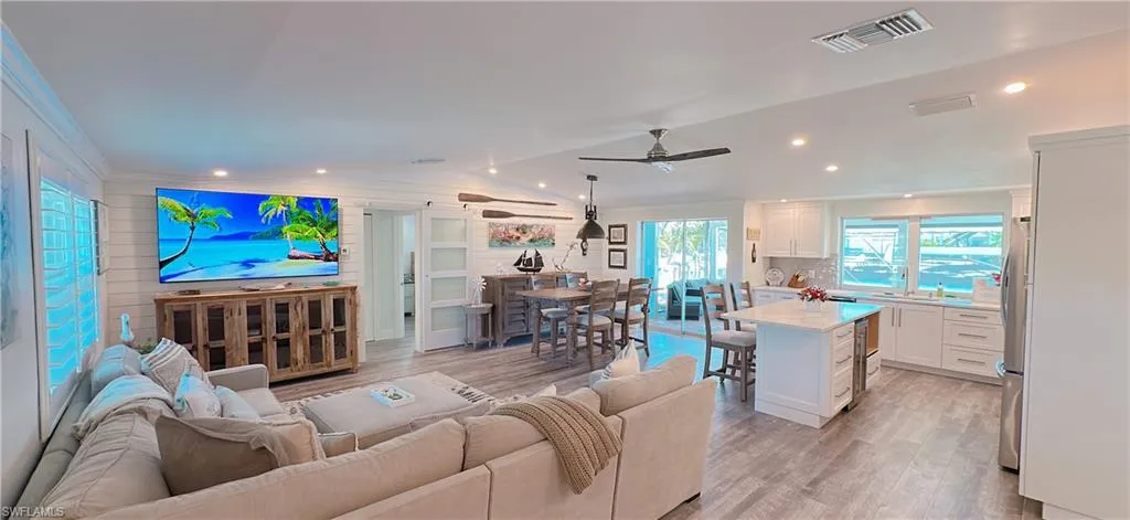Living area featuring a ceiling fan, visible vents, light wood-style flooring, vaulted ceiling, and crown molding