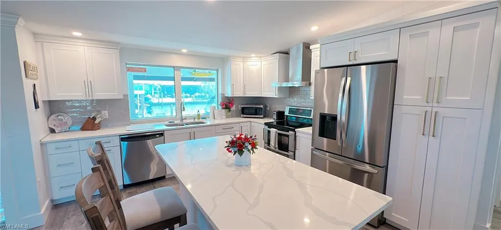 Kitchen with a sink, decorative backsplash, appliances with stainless steel finishes, white cabinetry, and wall chimney range hood