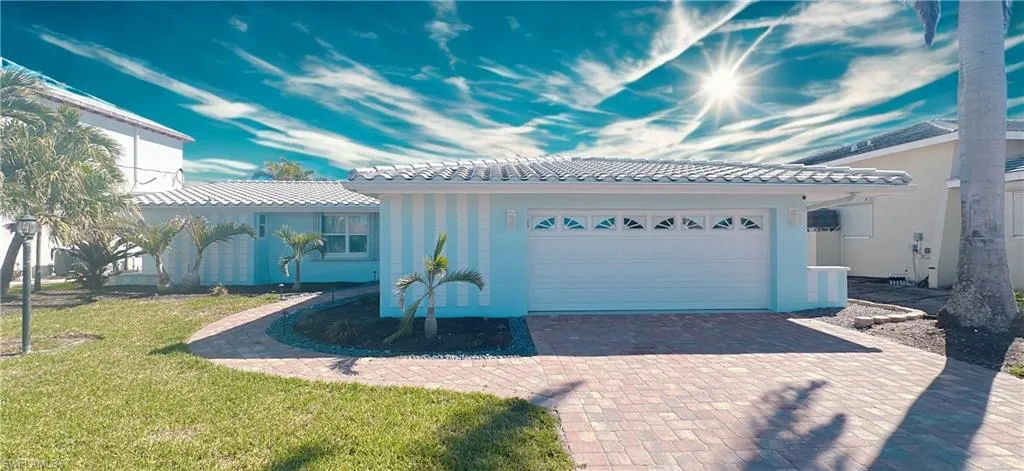 View of front facade with decorative driveway, a tiled roof, a front yard, an attached garage, and stucco siding
