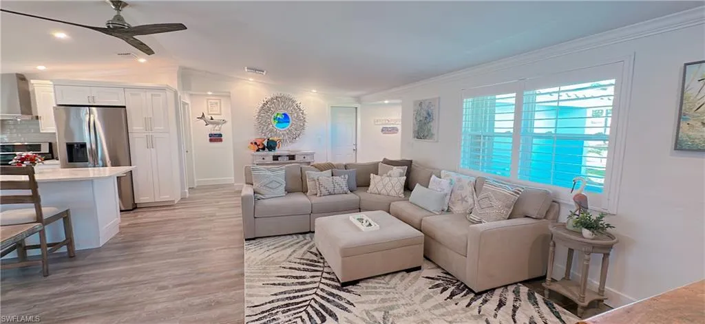 Living room with a ceiling fan, visible vents, light wood finished floors, lofted ceiling, and crown molding