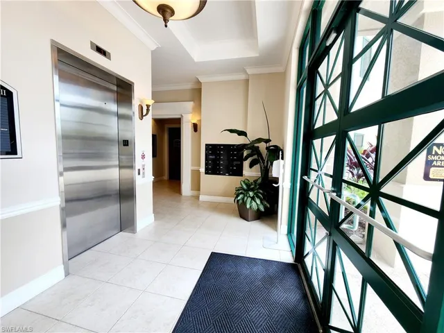 Foyer featuring elevator, mail area, a raised ceiling, light tile patterned flooring, and ornamental molding