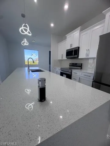 Kitchen featuring sink, hanging light fixtures, light stone counters, white cabinets, and range