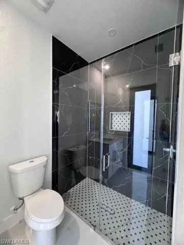 Bathroom with a textured ceiling, toilet, and an enclosed shower