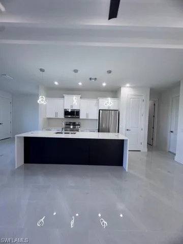 Kitchen with white cabinets, decorative light fixtures, a large island, and fridge
