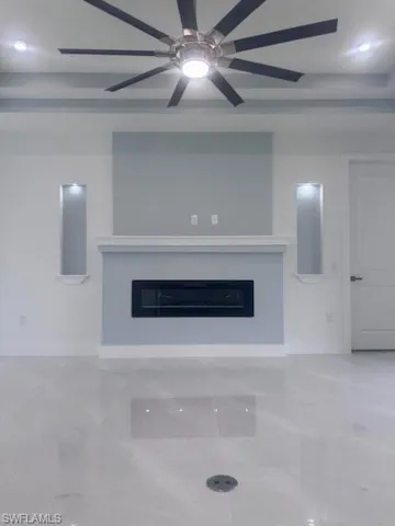 Unfurnished living room with a glass covered fireplace, a ceiling fan, and baseboards