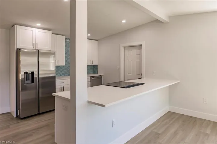 Kitchen featuring light hardwood / wood-style flooring, kitchen peninsula, stainless steel appliances, backsplash, and white cabinets