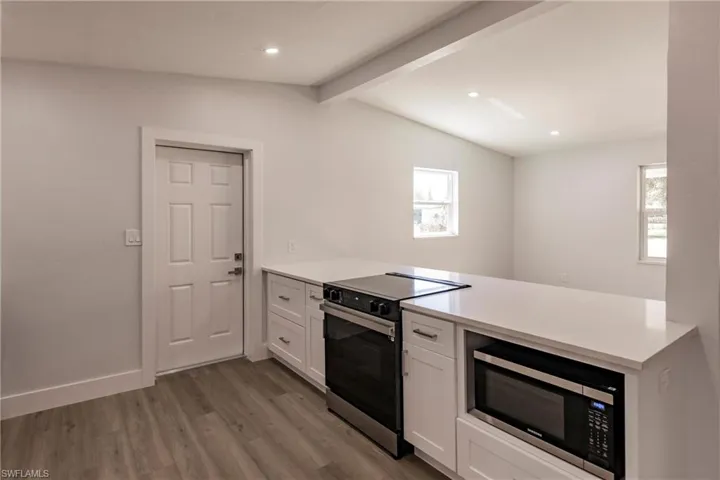 Kitchen with stainless steel appliances, a healthy amount of sunlight, white cabinets, and lofted ceiling with beams