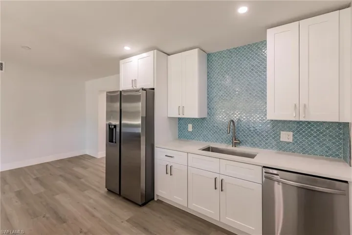 Kitchen with stainless steel appliances, backsplash, white cabinetry, light wood-type flooring, and sink