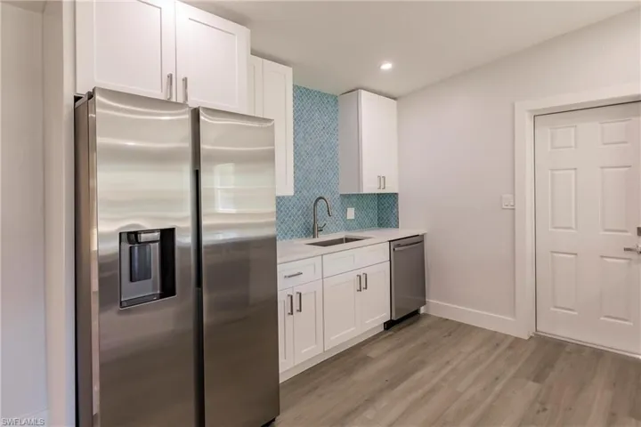 Kitchen with light hardwood / wood-style floors, stainless steel appliances, tasteful backsplash, white cabinets, and sink