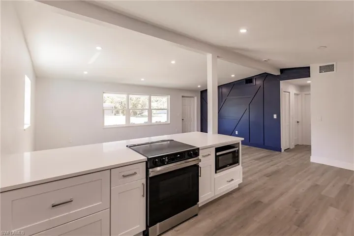 Kitchen with electric stove, light wood-type flooring, white cabinetry, and black microwave