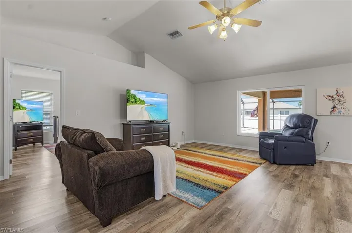 Living room featuring baseboards, vaulted ceiling, visible vents, ceiling fan, and wood finished floors