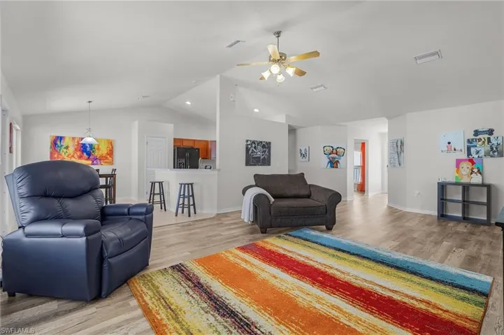 Living room with light wood-style floors, a ceiling fan, visible vents, lofted ceiling, and baseboards