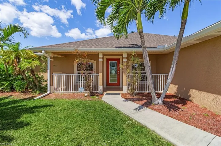 Property entrance featuring roof with shingles, covered porch, a lawn