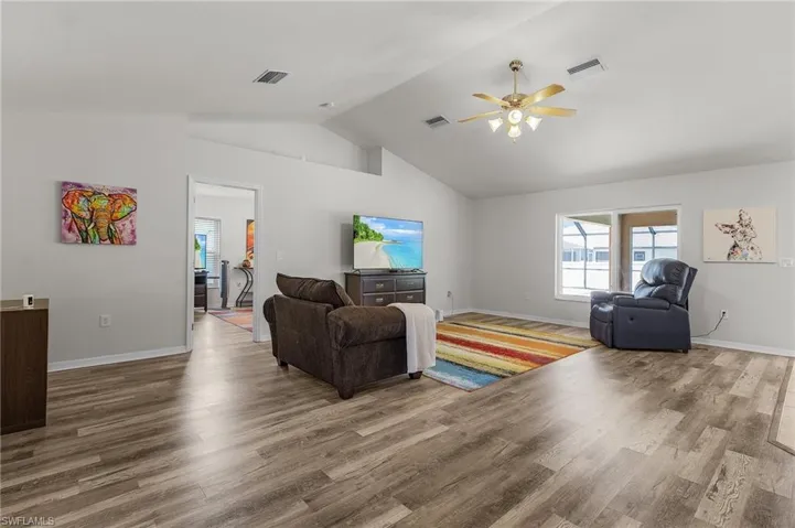 Living area featuring baseboards, vaulted ceiling, a ceiling fan, and wood finished floors