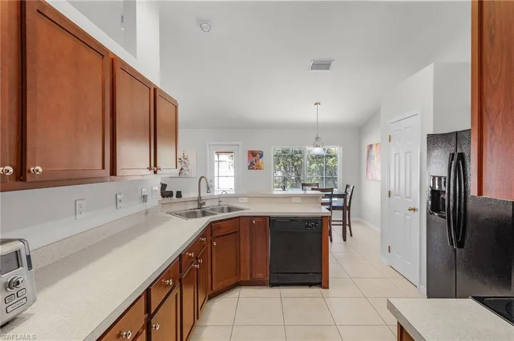 Kitchen featuring a peninsula, light tile patterned floors, black appliances, visible vents, and a sink