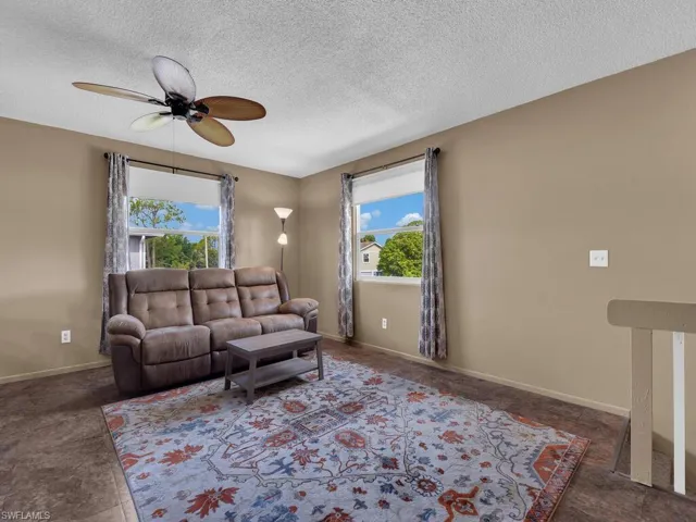 Living area with ceiling fan, a textured ceiling, and baseboards
