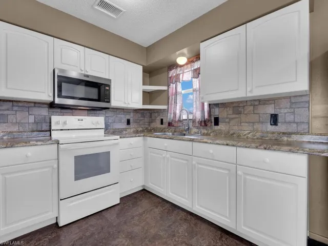 Kitchen with stainless steel microwave, electric stove, a sink, white cabinetry, and a textured ceiling