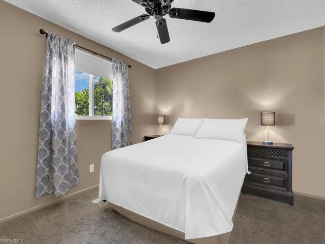 Carpeted bedroom with a textured ceiling, baseboards, and a ceiling fan