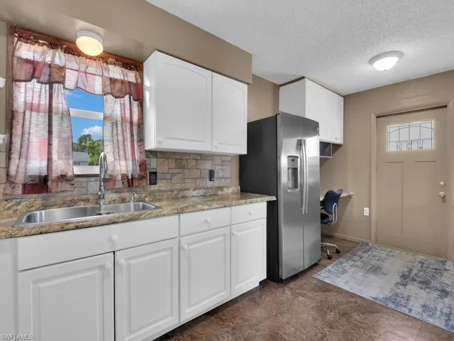 Kitchen with a sink, stainless steel fridge with ice dispenser, healthy amount of natural light, tasteful backsplash, and a textured ceiling