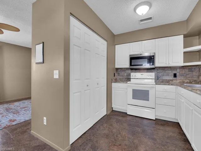 Kitchen with stainless steel microwave, electric range, a textured ceiling, open shelves, and backsplash