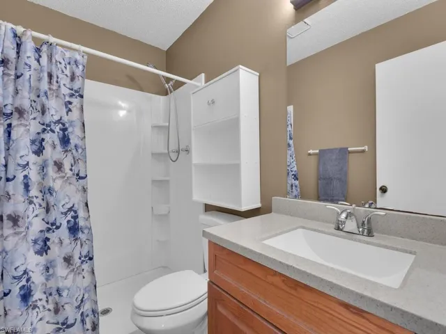 Bathroom with toilet, vanity, a shower with curtain, and a textured ceiling