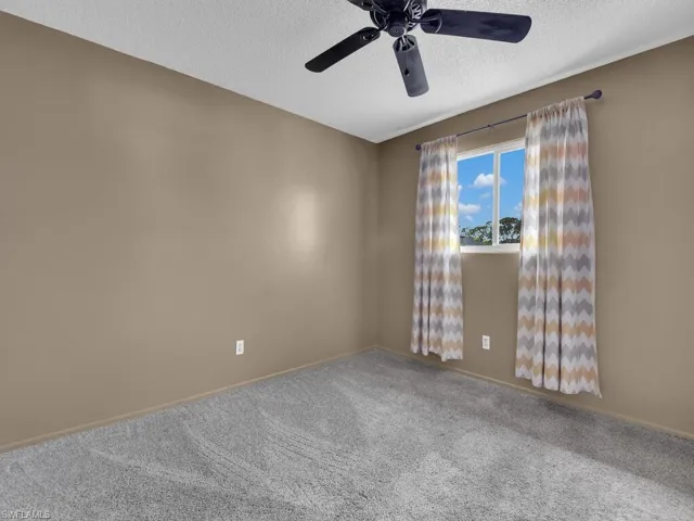 Carpeted empty room with a textured ceiling, a ceiling fan, and baseboards