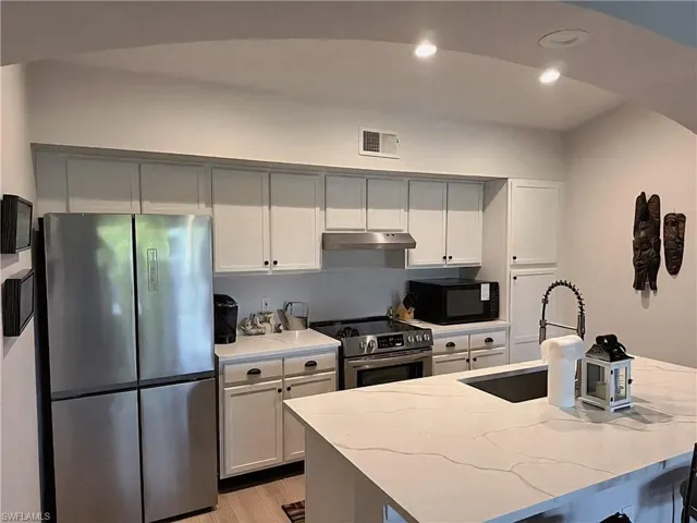 Kitchen with recessed lighting, appliances with stainless steel finishes, a kitchen bar, white cabinets, and light wood finished floors