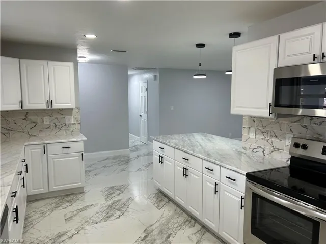 Kitchen with white cabinets, appliances with stainless steel finishes, tasteful backsplash, and pendant lighting