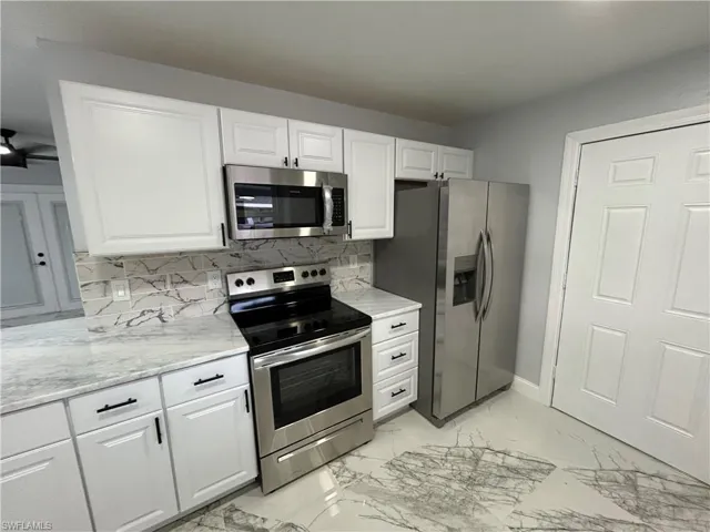Kitchen with white cabinets, appliances with stainless steel finishes, tasteful backsplash, and light tile flooring