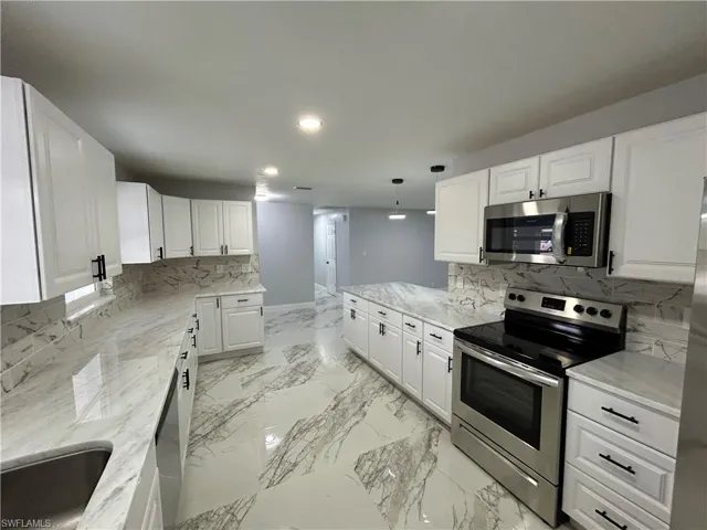 Kitchen featuring backsplash, appliances with stainless steel finishes, white cabinetry, and light stone counters