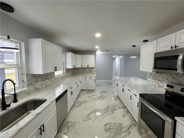 Kitchen with stainless steel appliances, white cabinets, light tile flooring, and pendant lighting