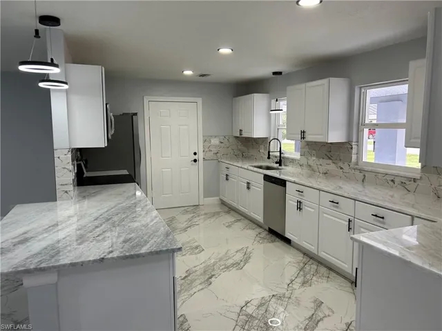Kitchen featuring appliances with stainless steel finishes, white cabinets, pendant lighting, sink, and tasteful backsplash