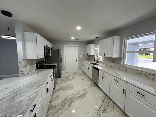 Kitchen featuring white cabinetry, appliances with stainless steel finishes, decorative light fixtures, tasteful backsplash, and light tile floors