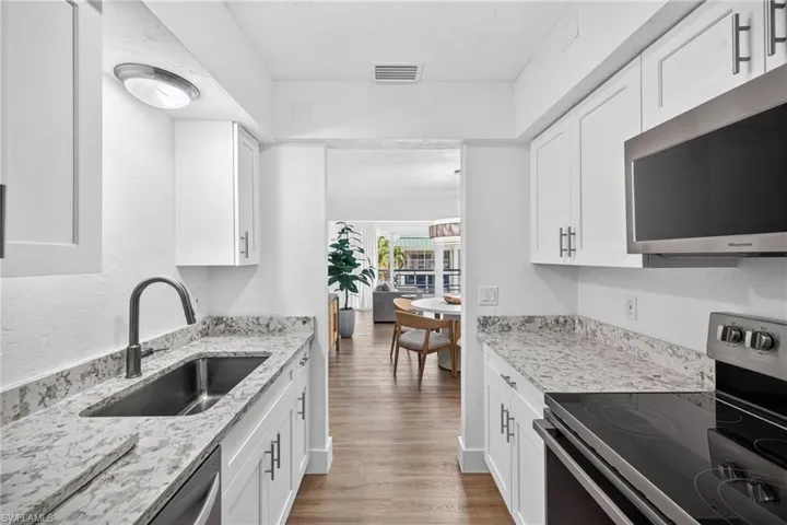 Galley kitchen featuring white cabinetry, light-toned countertops, stainless steel appliances including an over-the-range microwave and electric range, and wood-finish flooring