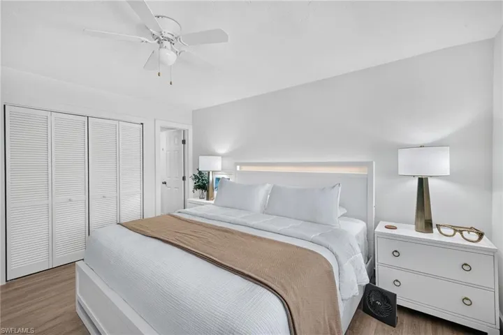 Bedroom featuring wood-finish flooring, louvered bi-fold closet doors, a ceiling fan with integrated lighting, and a white paneled headboard with accent lighting